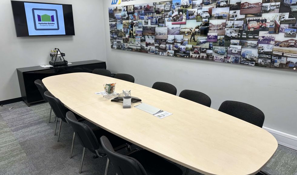 Conference room with an oval table, chairs, a wall-mounted TV, and a collage of company history photos labelled 'Hampsons History