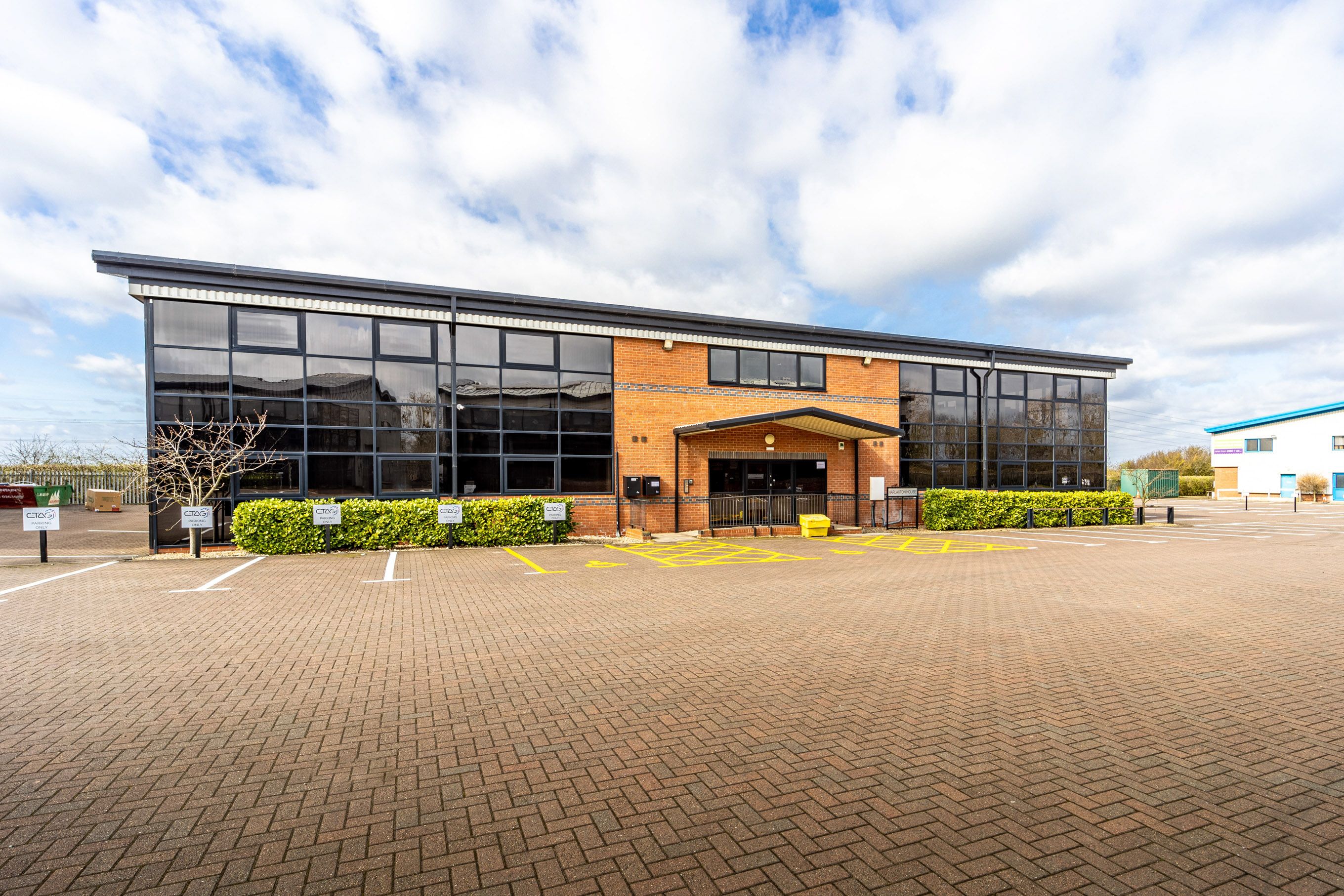 Exterior of a modern brick office building with large glass windows and an empty car park in front